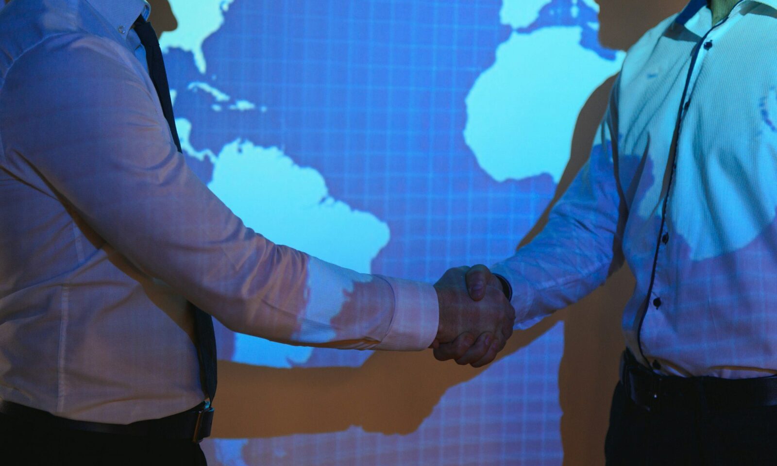 handshake-with-map-of-the-world-in-background-two-businessmen-on-the-background-of-the-world-map