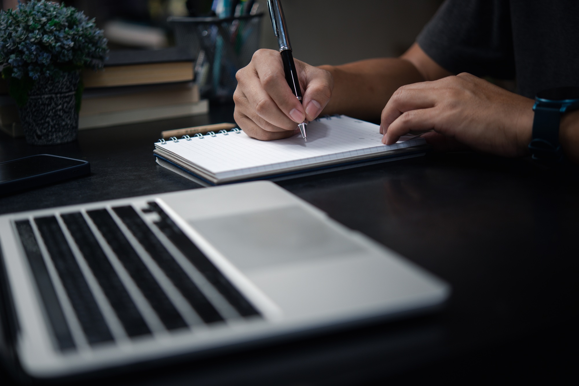 Man hand writing on notebook with computer laptop.Business planning, E learning, journal concept.