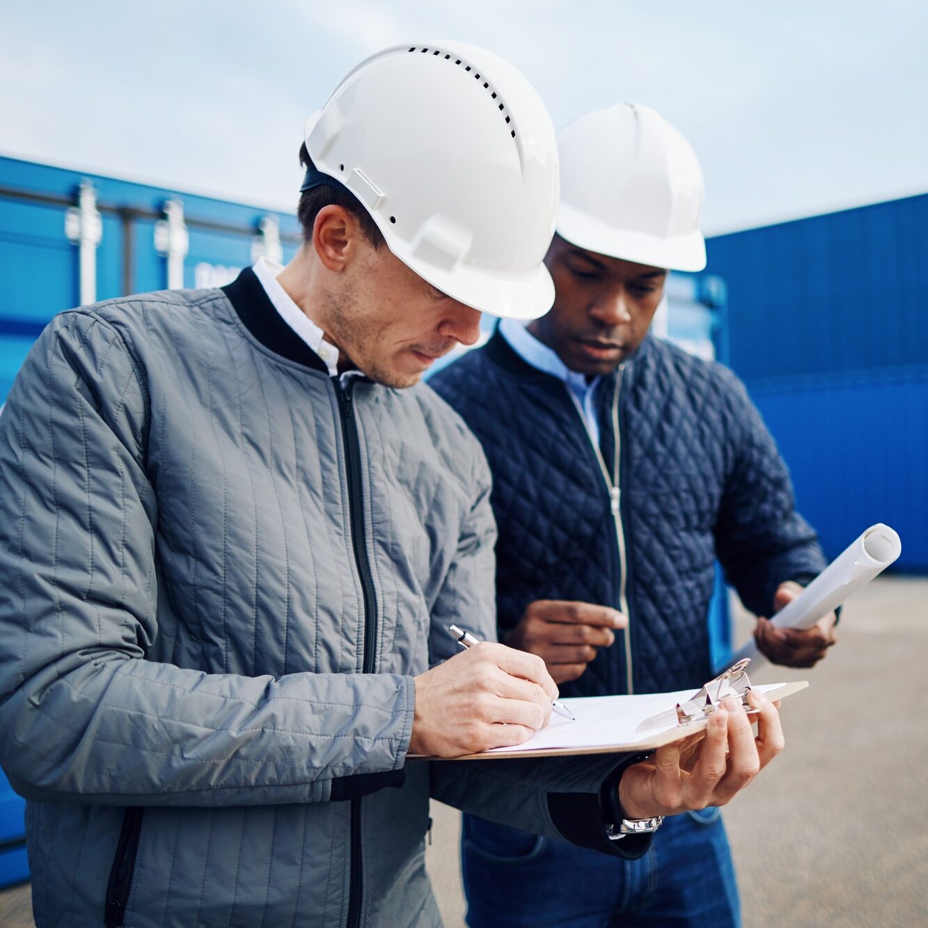 Two engineers standing in a shipping yard discussing logistics