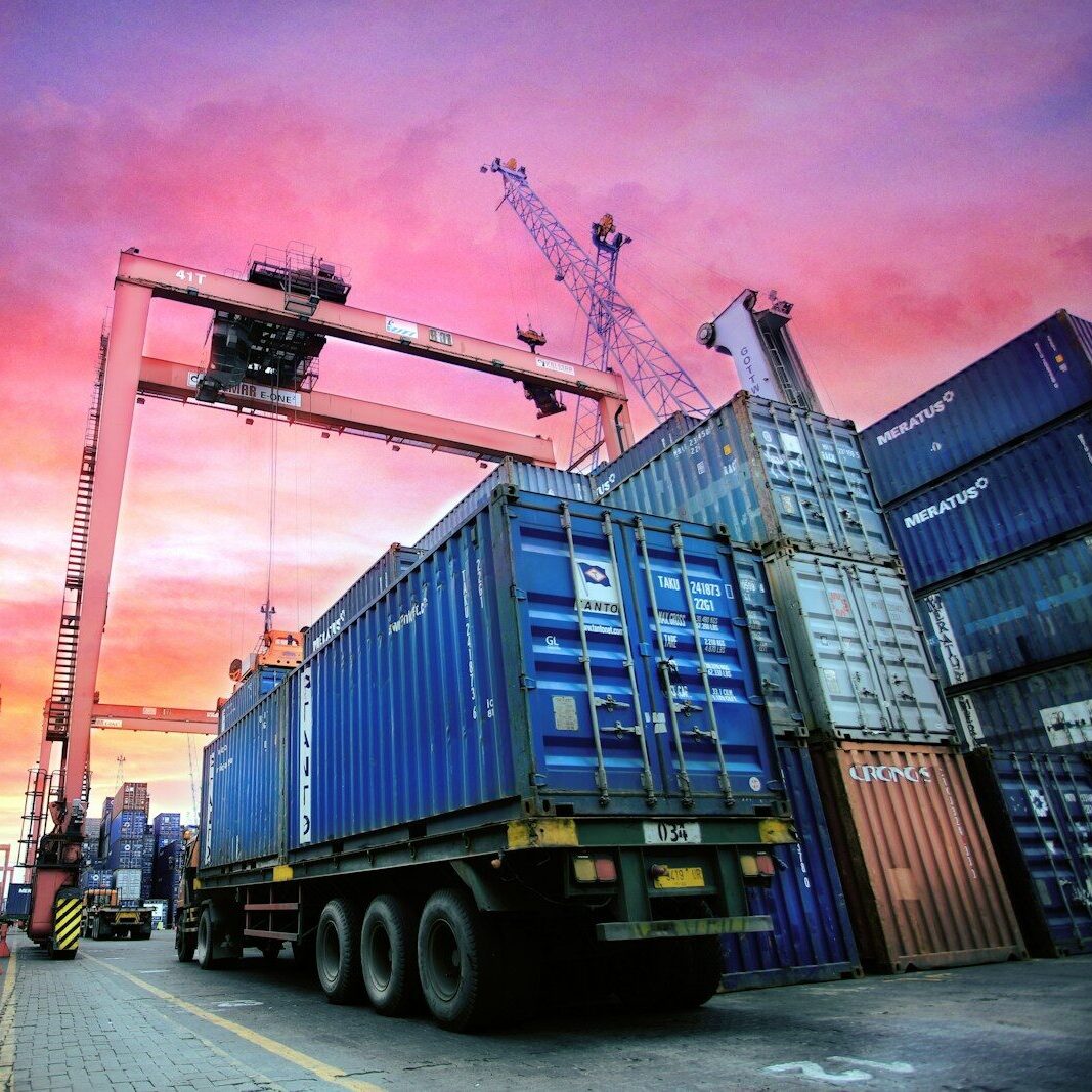 Shipping containers stacked at a busy port at sunset.